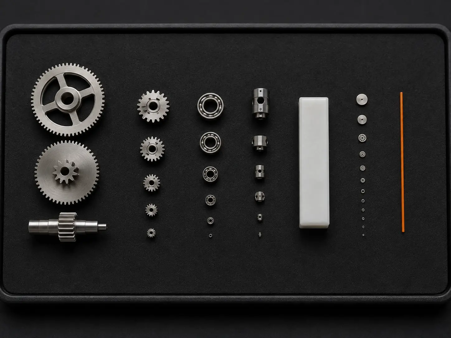 Precision components arranged from large to microscopic on a black inspection tray